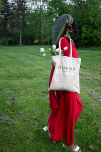 Girl walking while looking away from camera wearing red maxi dress and carrying tote bag with tulips.