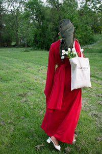 Girl walking while looking away from camera wearing red maxi dress and carrying tote bag with tulips.