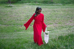 Girl walking on grass towards camera wearing red maxi dress and carrying tote bag with tulips.