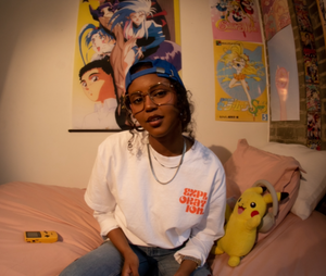 Girl in anime-themed room wearing backward blue cap and oversized tee