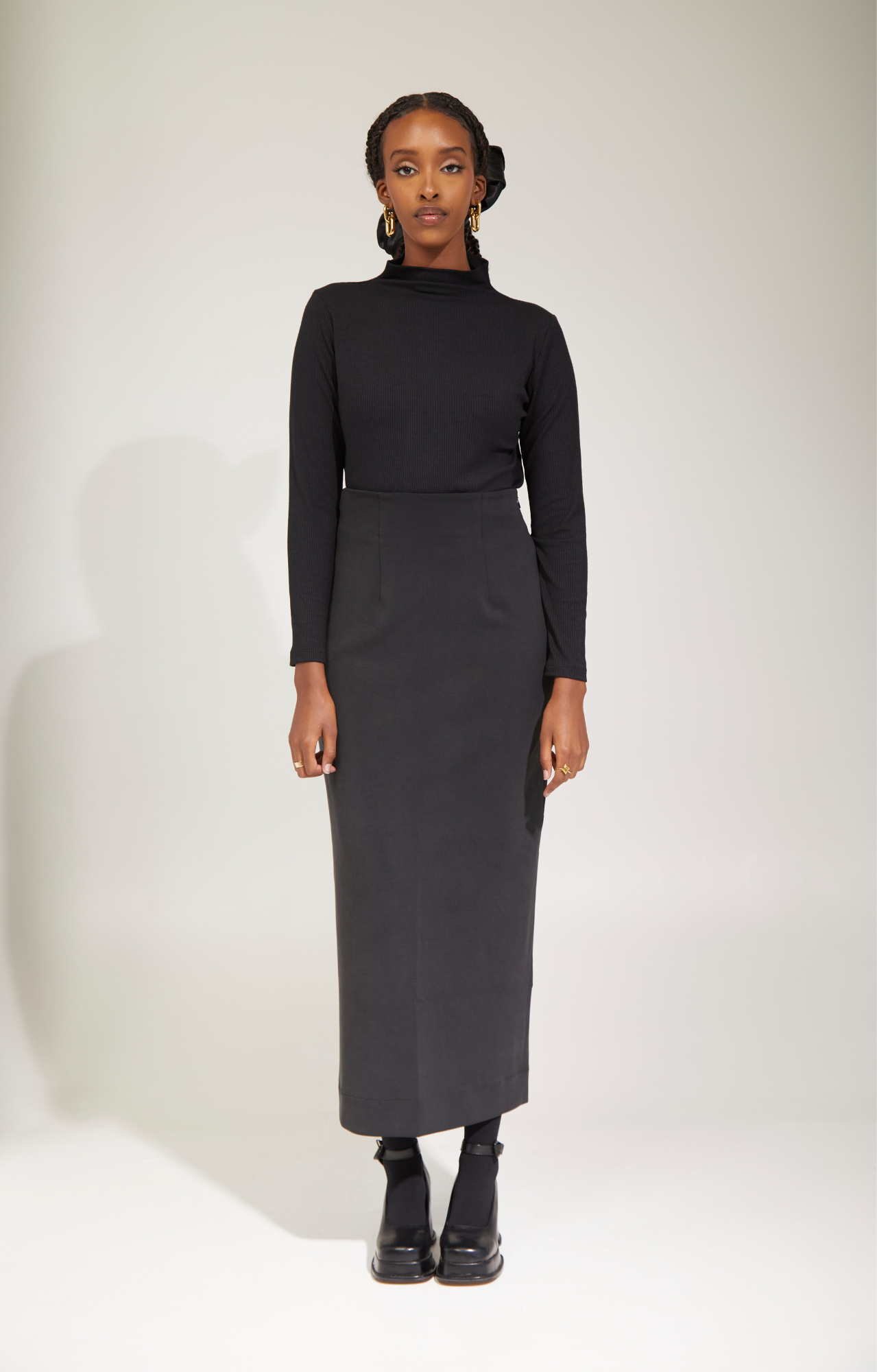 Woman standing wearing black mock neck long sleeve and high waisted maxi pencil skirt.